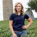 Female standing in green field. Silo behind.