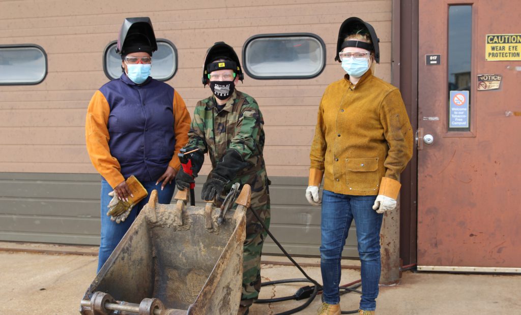 Three students stand by their welding project