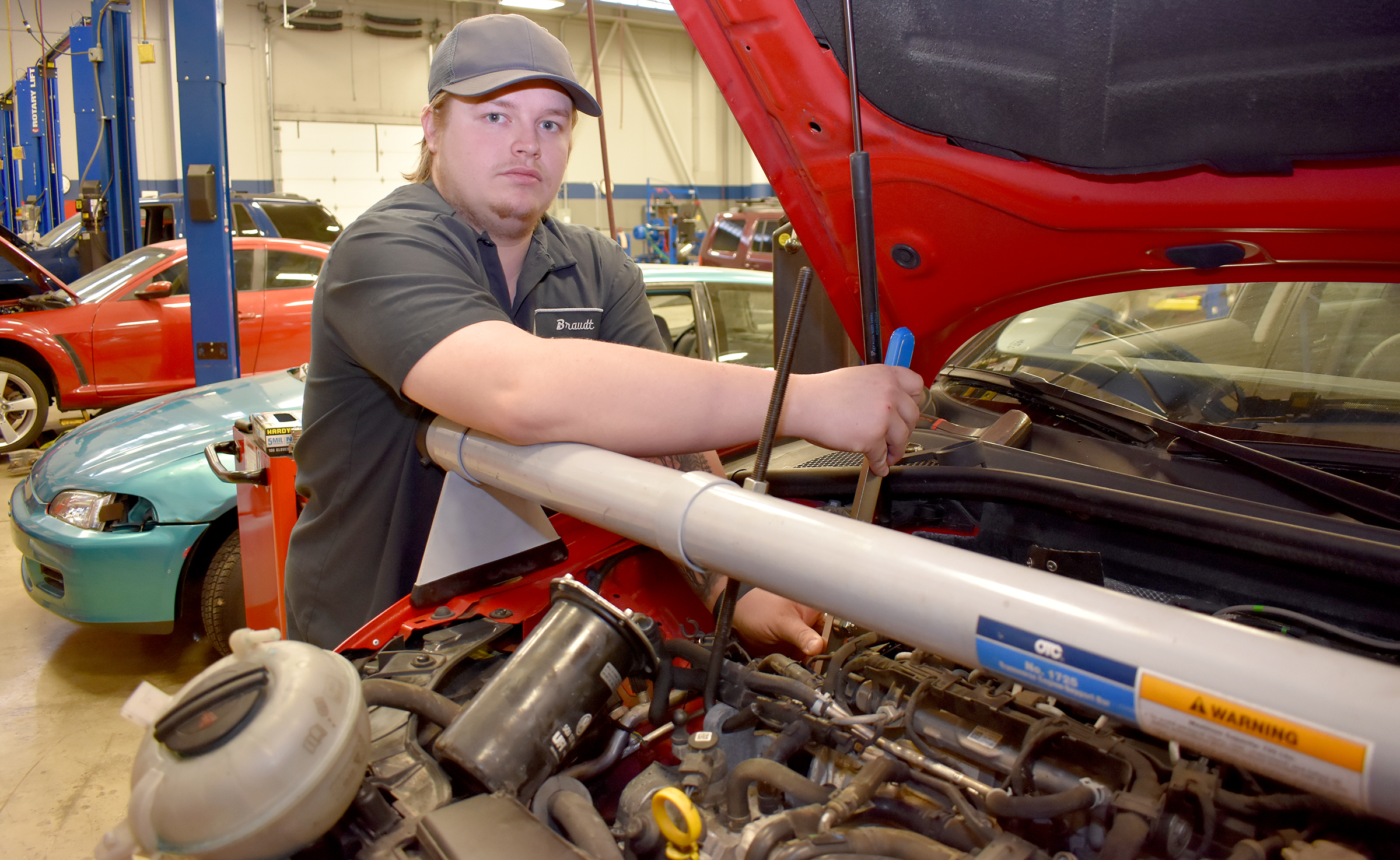 Male student next to vehicle with open hood.