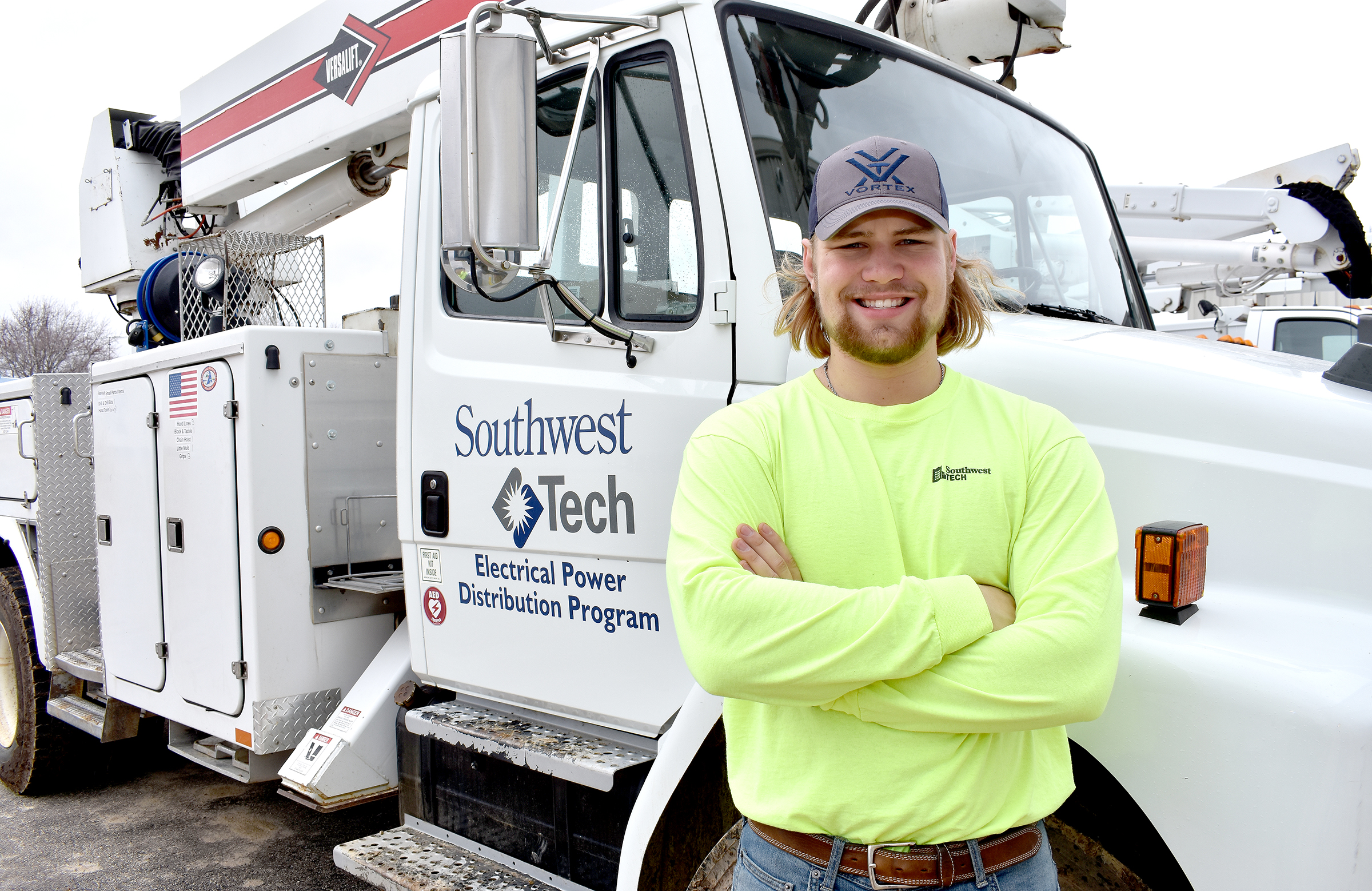 Male student with hat on standing in front of utility truck.