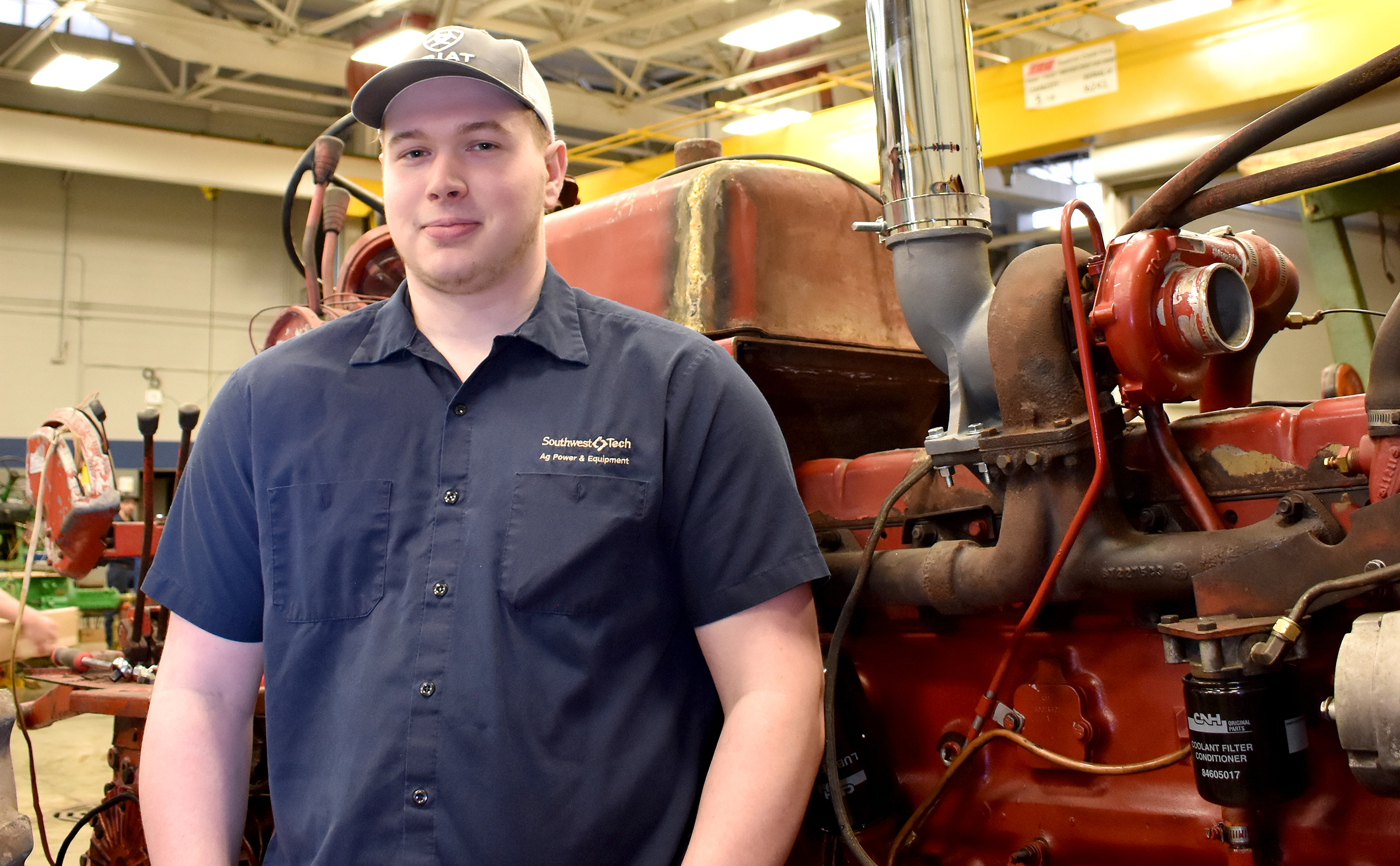 Male ag student standing in front of older red tractor.