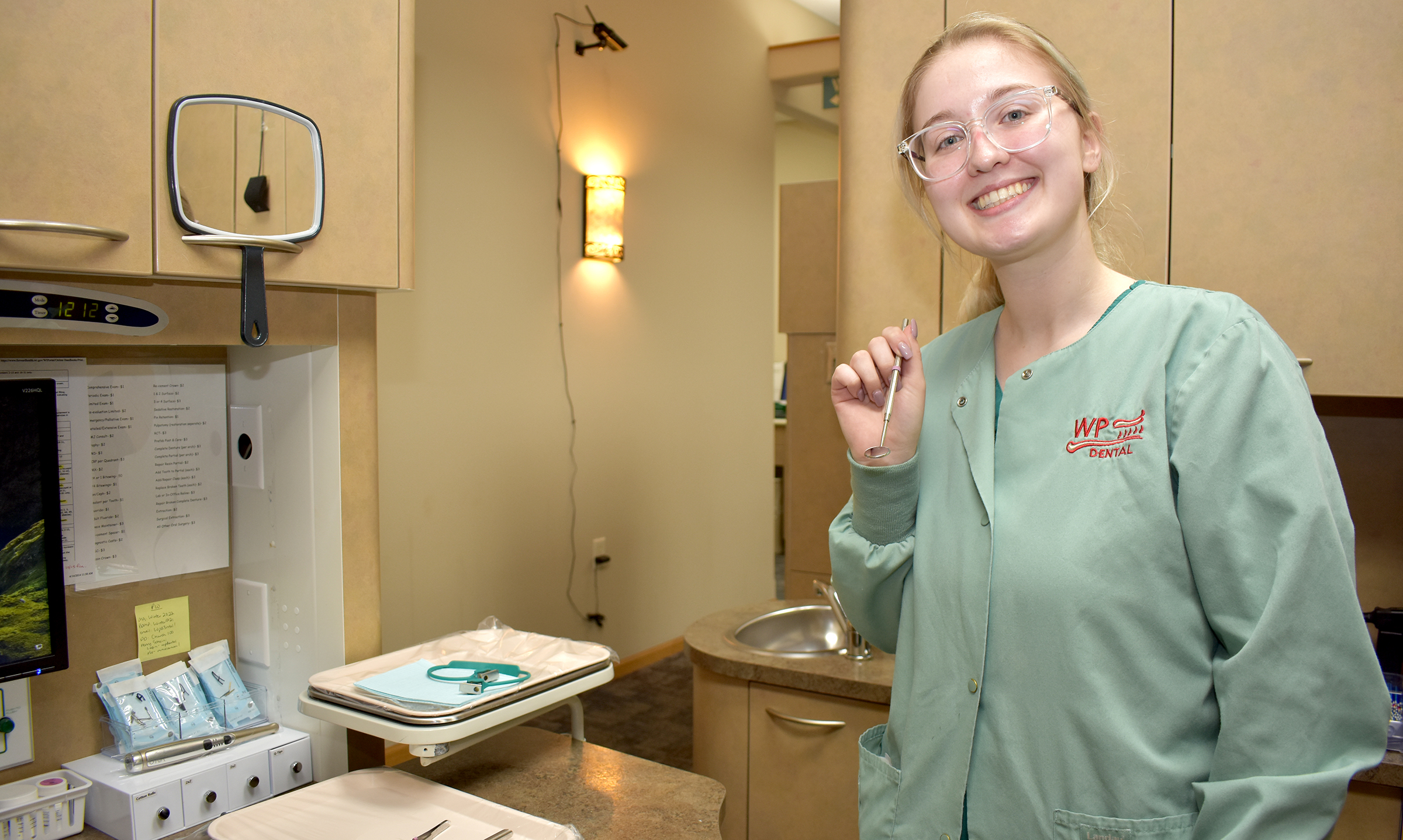 Dental student smiling at work, holding work instrument.