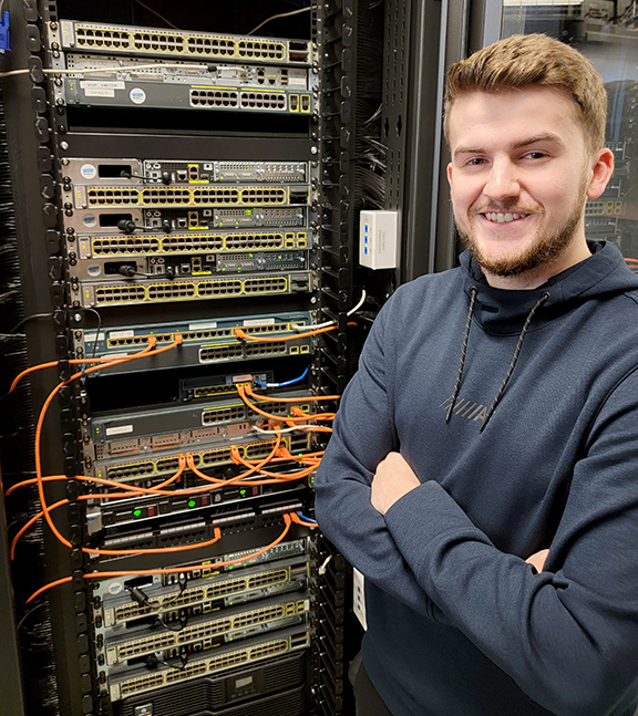 Male student standing next to computer servers.