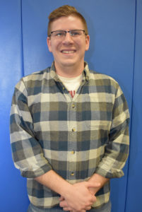 Male student standing in front of blue wall.