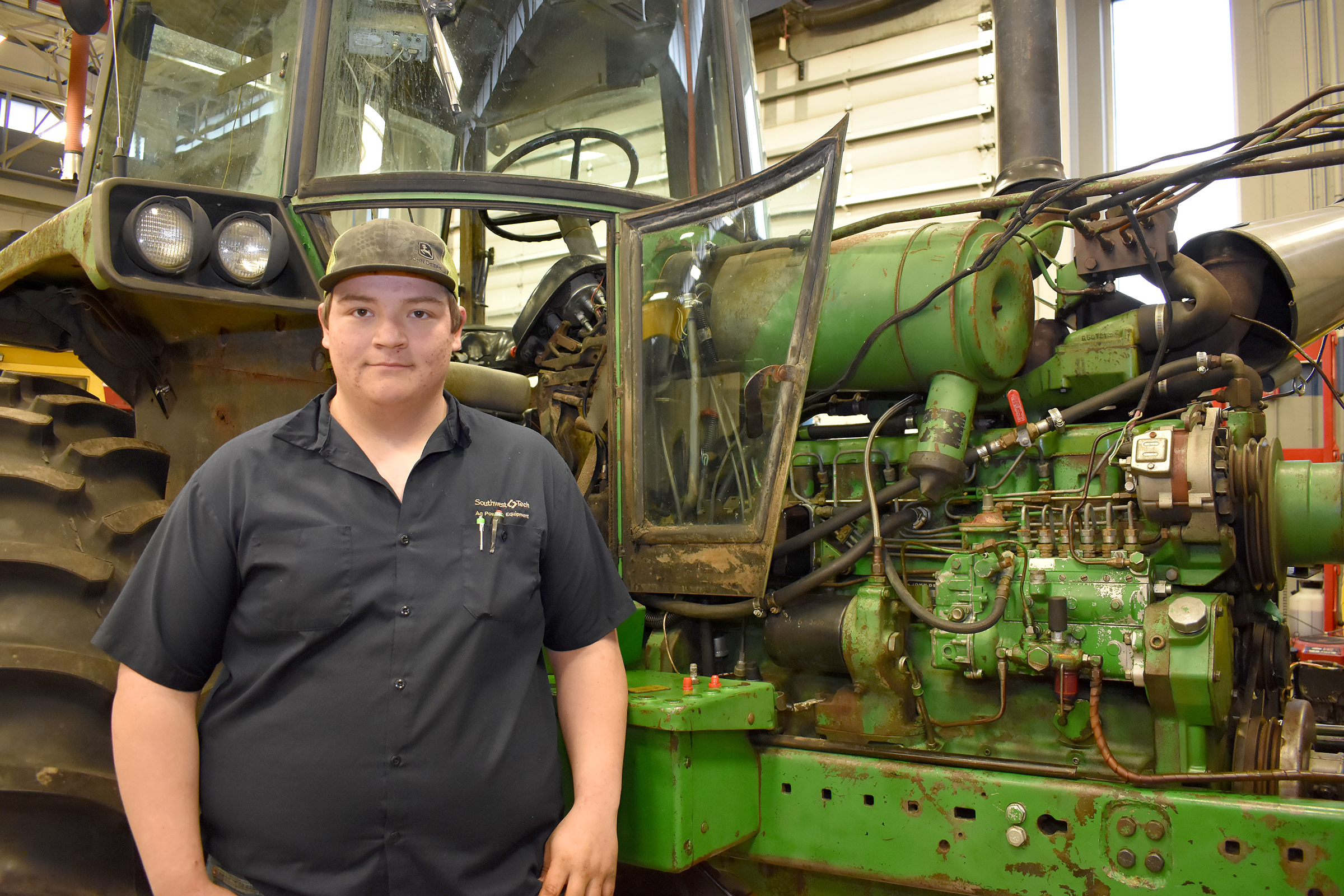 Male ag power student standing in front of green tractor.