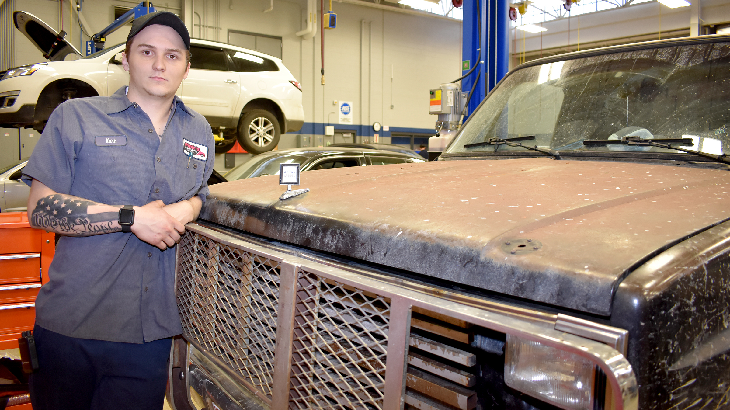 Male student standing next to truck hood.