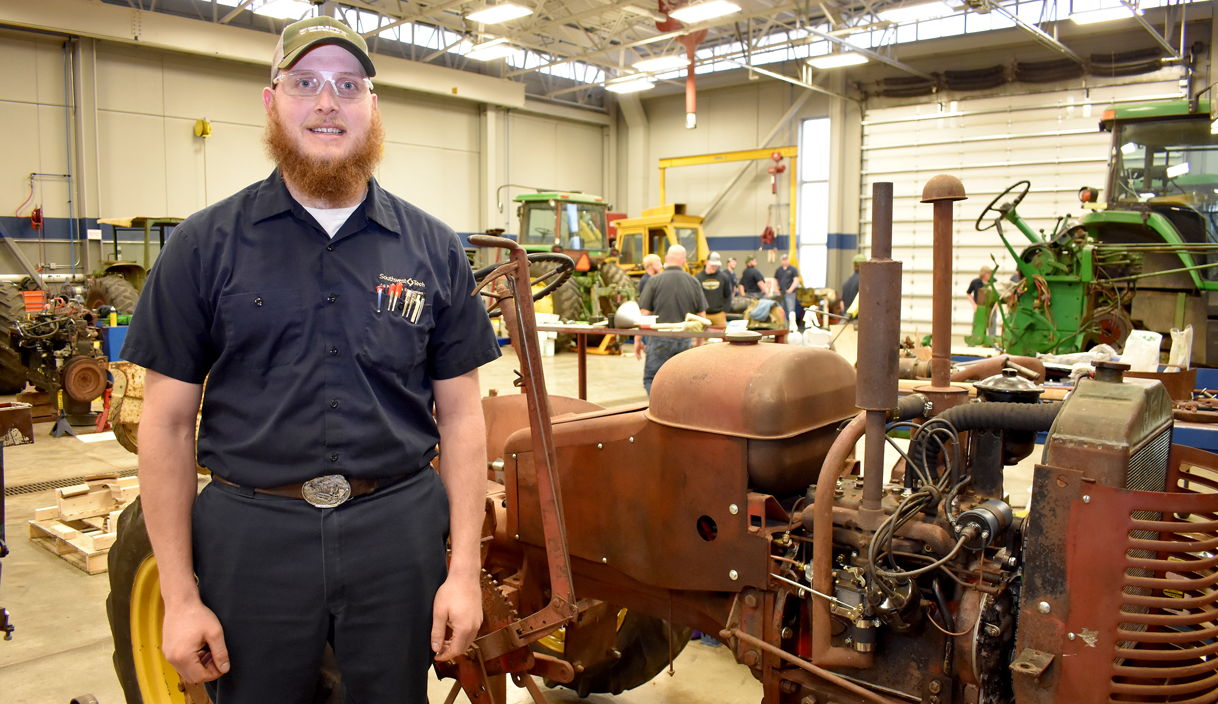 Male student standing in front of vintage red tractor.