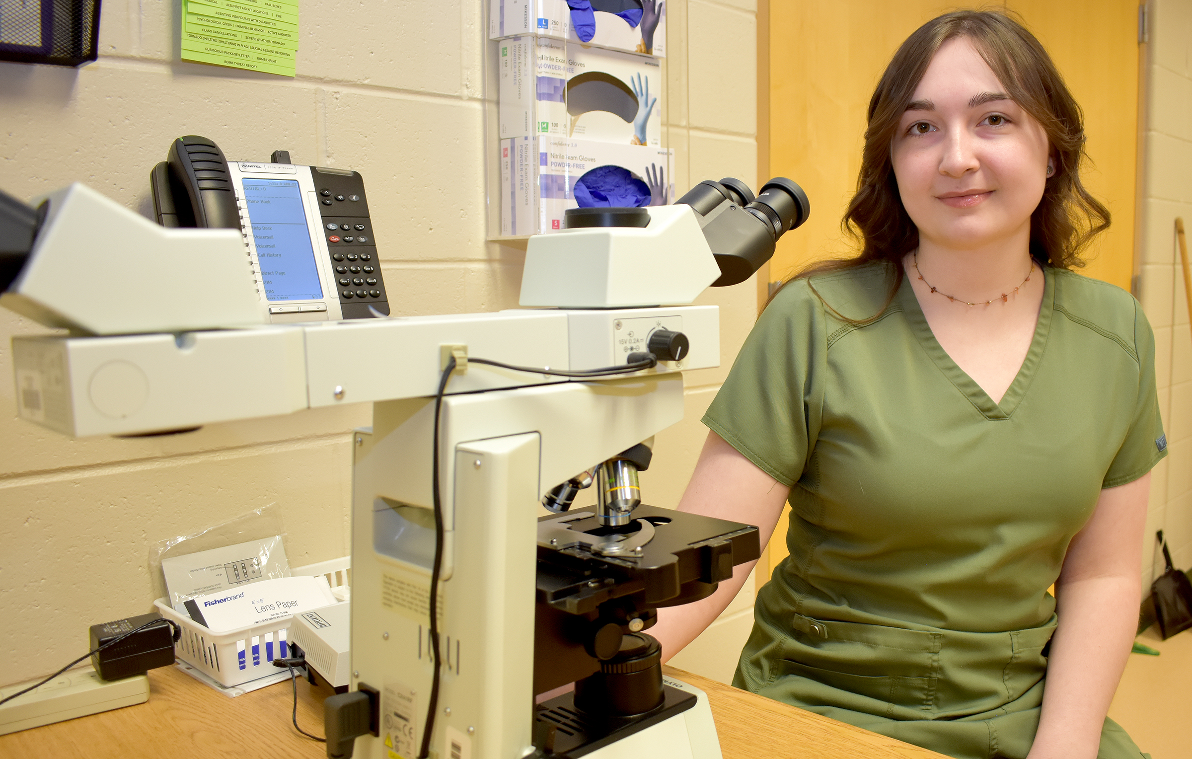 Female student sitting next to microscope.