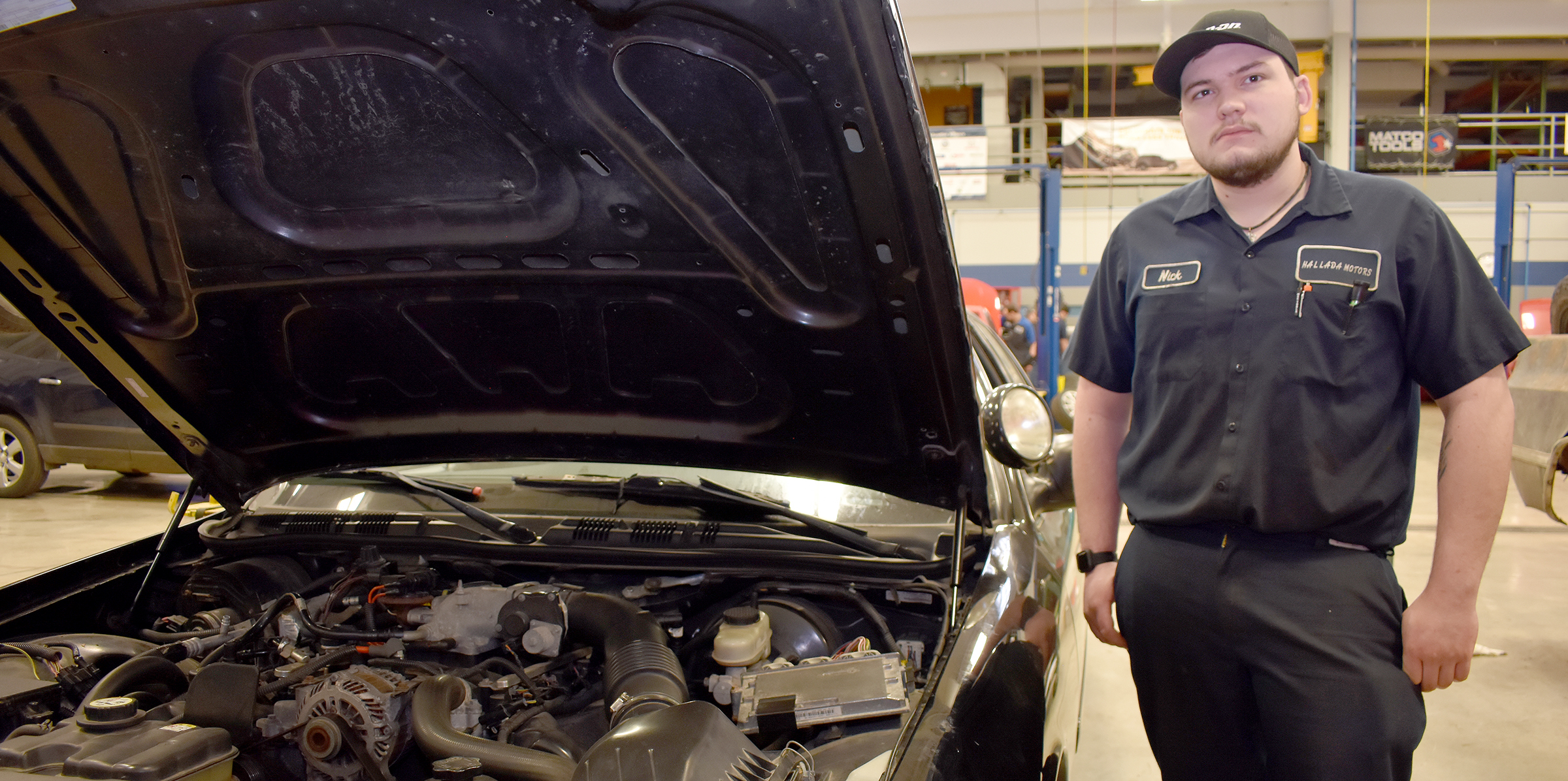 Male student standing next to vehicle with hood open.