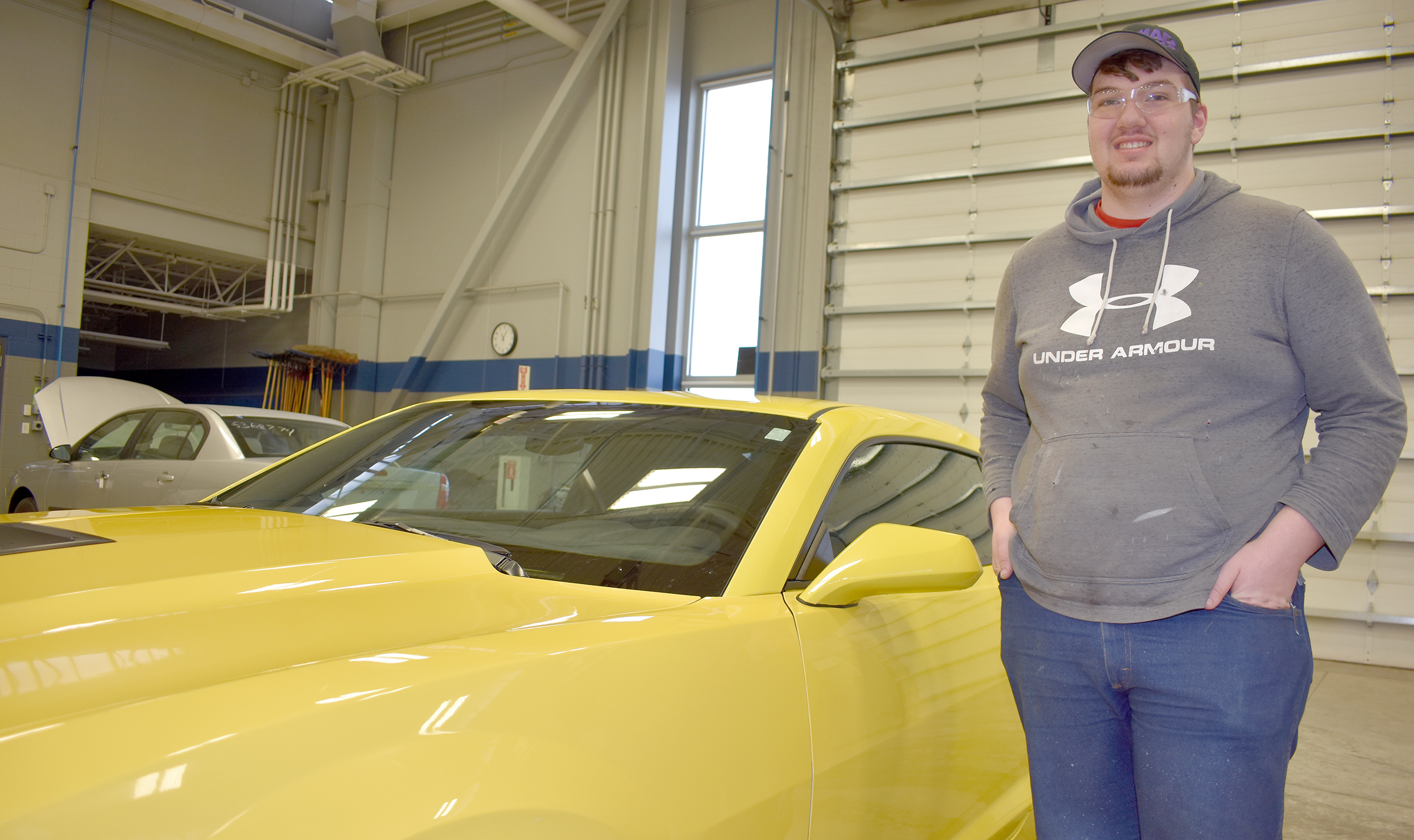 Mmale student standing next to yellow Camaro.