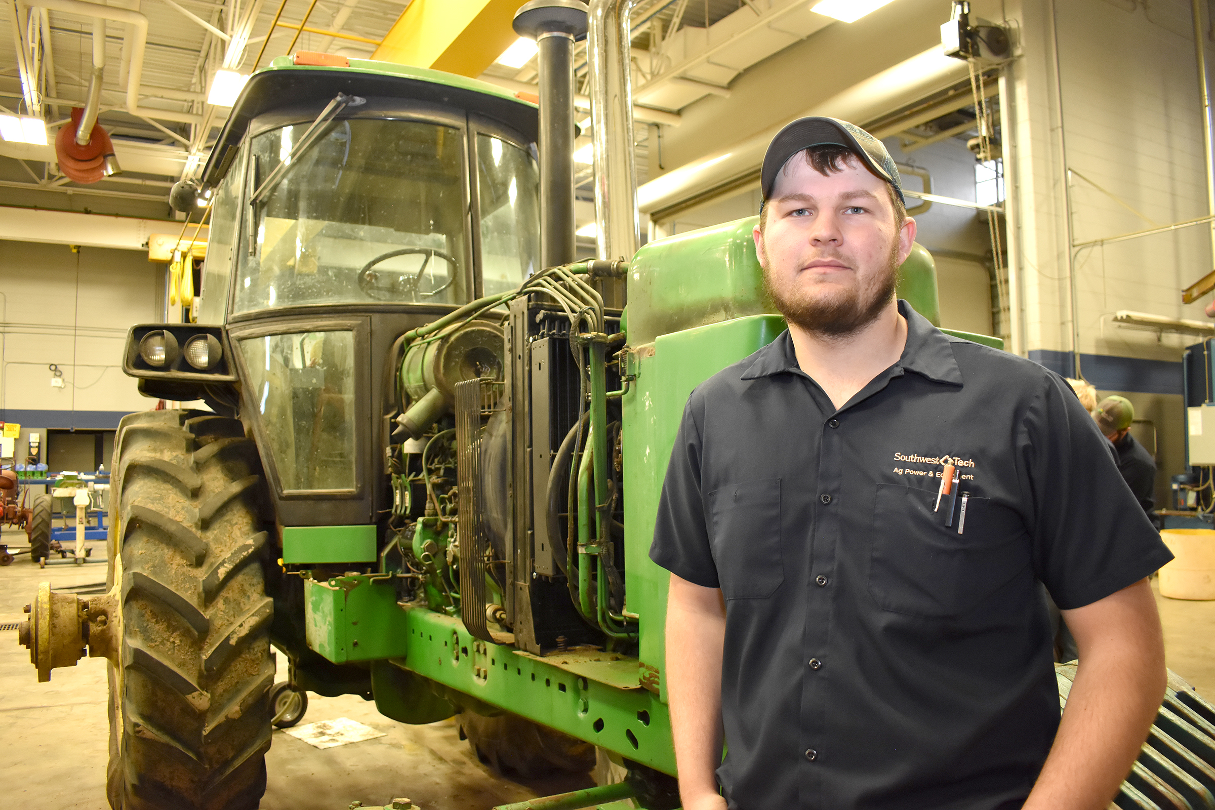 Male student standing in front of green tractor.