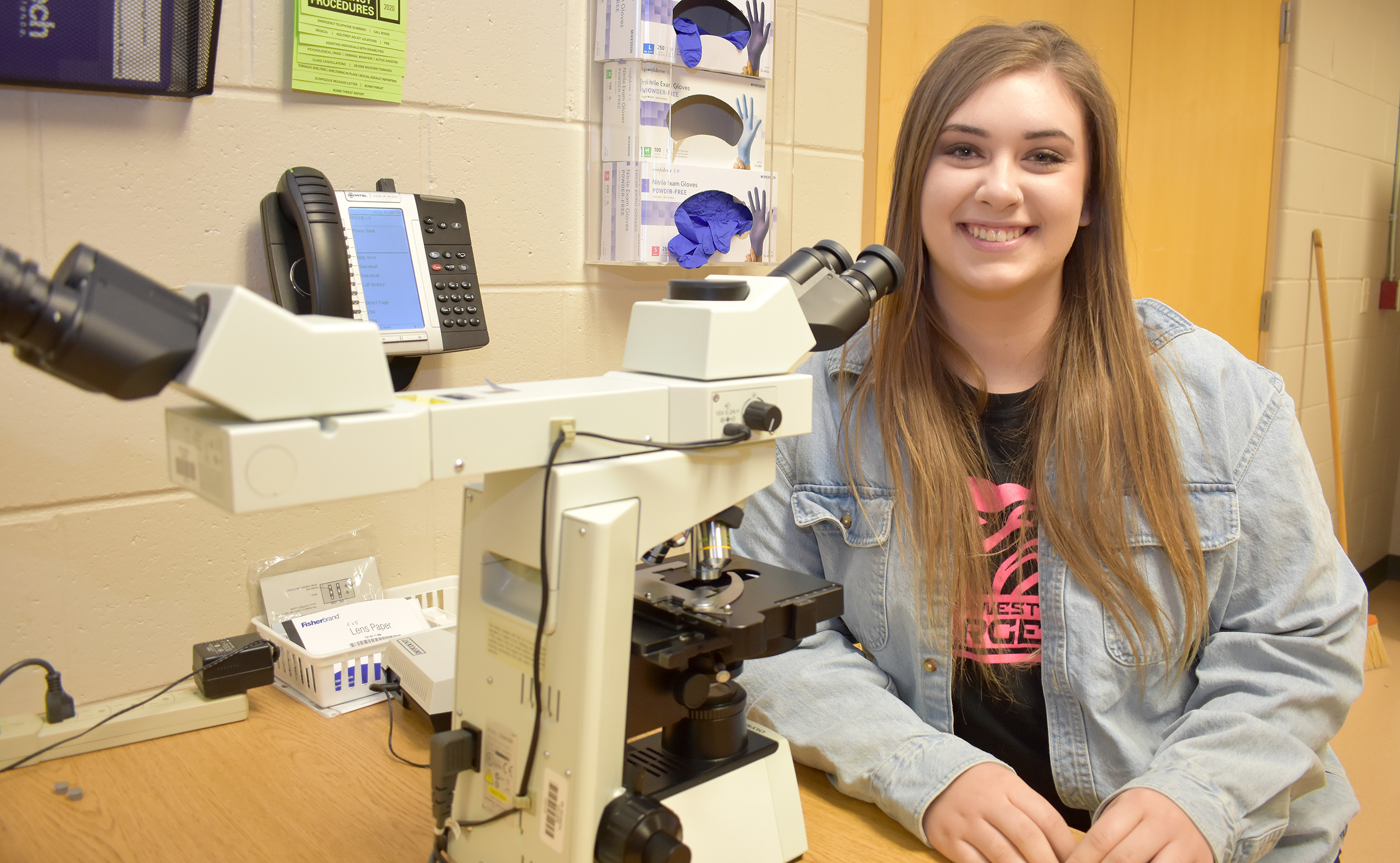 Female student sitting by microscope.