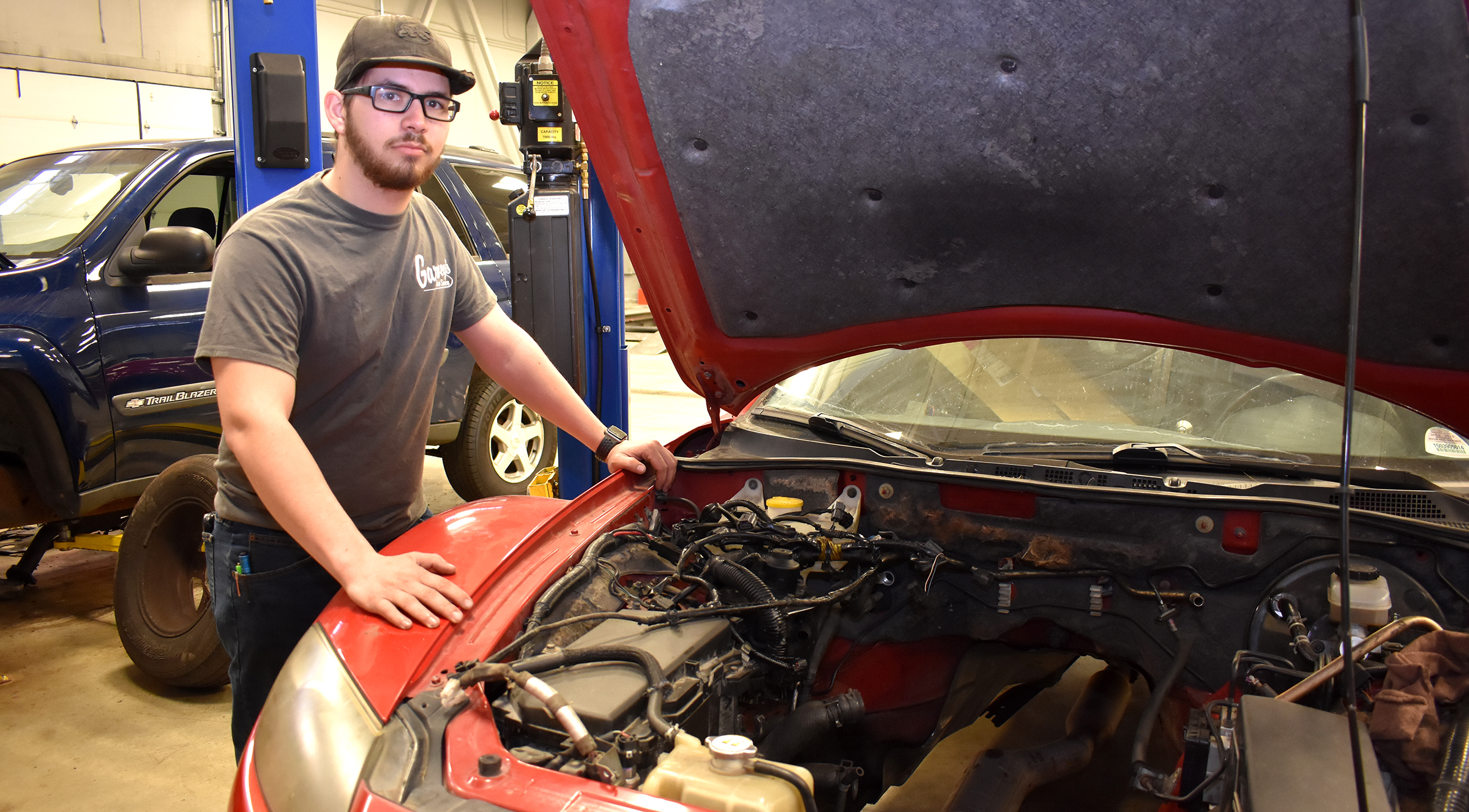 Male student next to vehicle with open hood.