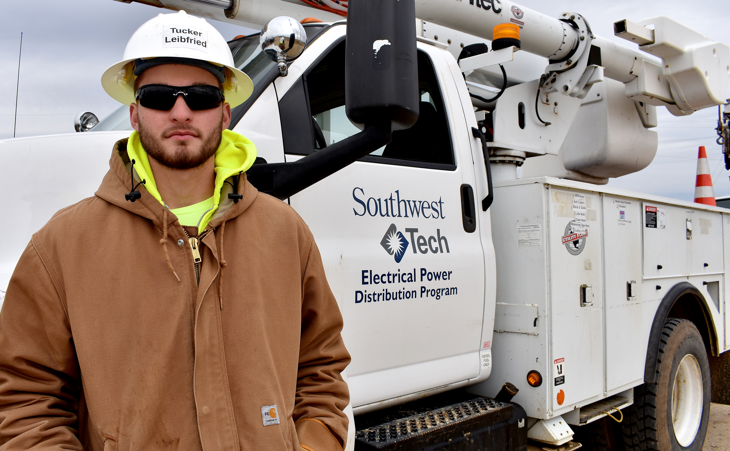 Lineman student standing in front of utility truck wearing white helmet.