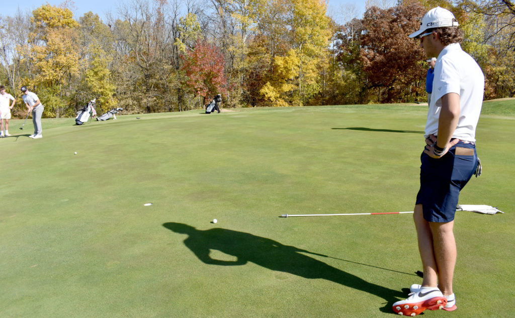 Two golfers on the green. One putting.